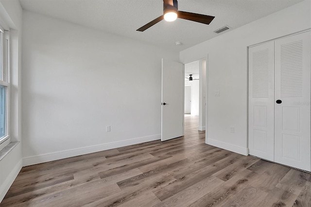 unfurnished bedroom with a closet, visible vents, a ceiling fan, wood finished floors, and baseboards