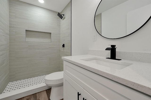 bathroom featuring a tile shower, vanity, toilet, and wood finished floors