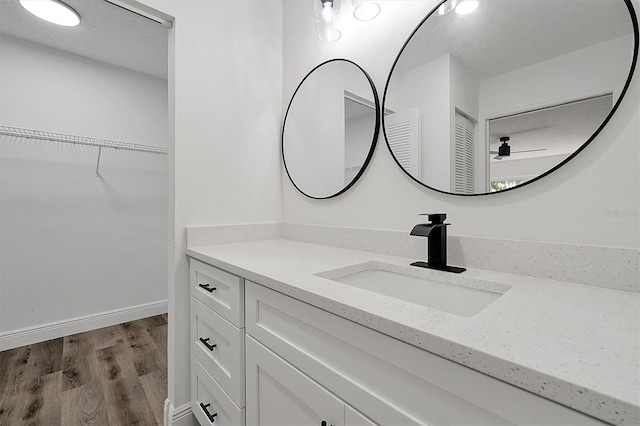 bathroom with a spacious closet, a textured ceiling, vanity, wood finished floors, and baseboards