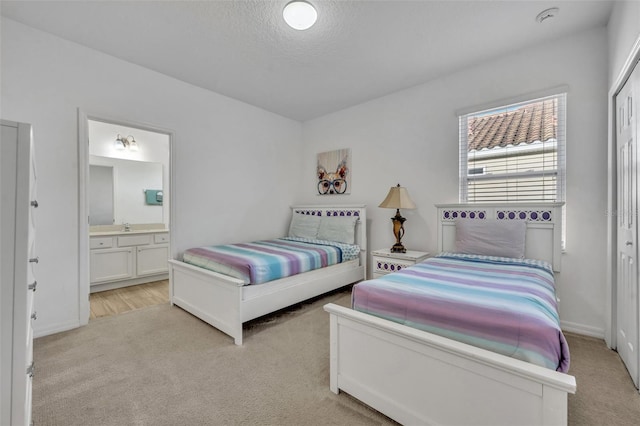 carpeted bedroom with ensuite bathroom, a closet, sink, and a textured ceiling