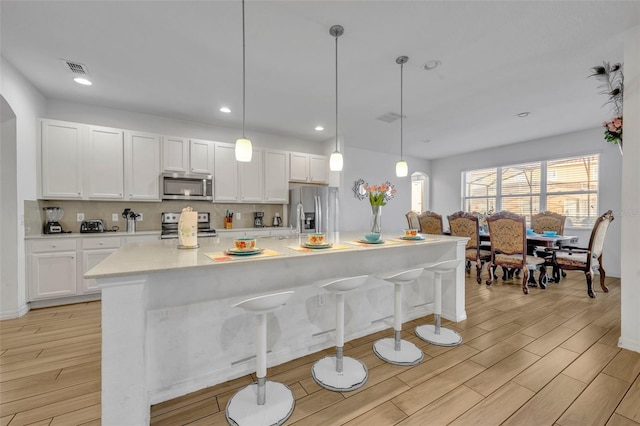 kitchen featuring white cabinetry, appliances with stainless steel finishes, a center island with sink, and decorative light fixtures