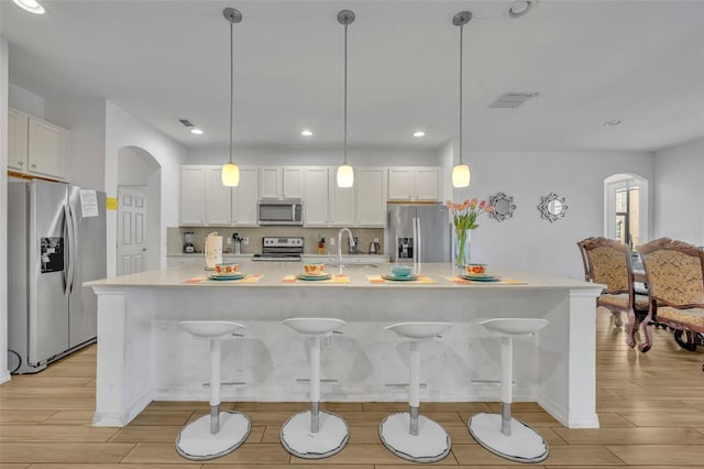 kitchen with an island with sink, a breakfast bar area, stainless steel appliances, hanging light fixtures, and white cabinets