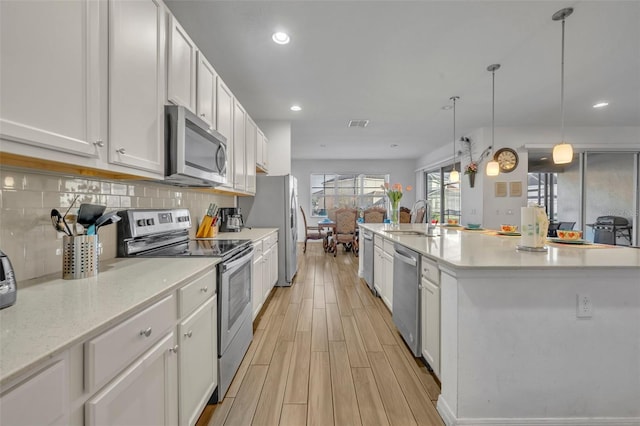 kitchen with stainless steel appliances, backsplash, hanging light fixtures, white cabinets, and sink