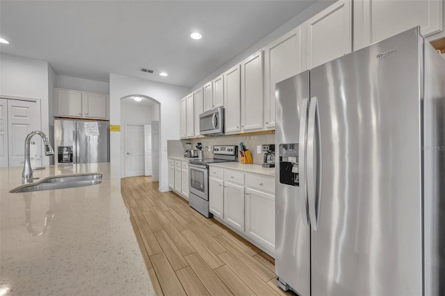 kitchen featuring decorative backsplash, sink, white cabinetry, appliances with stainless steel finishes, and light stone counters