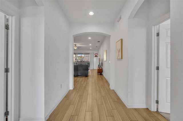 hall featuring light wood-type flooring, baseboards, arched walkways, and recessed lighting