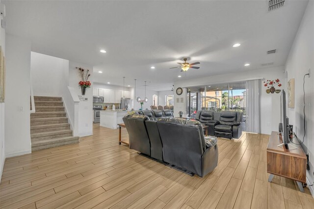 living area featuring stairway, visible vents, light wood finished floors, and a ceiling fan