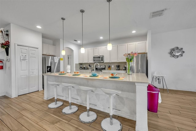 kitchen featuring arched walkways, an island with sink, decorative light fixtures, light countertops, and white cabinetry