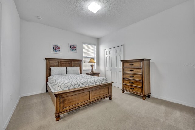 bedroom featuring a closet, light carpet, a textured ceiling, and baseboards