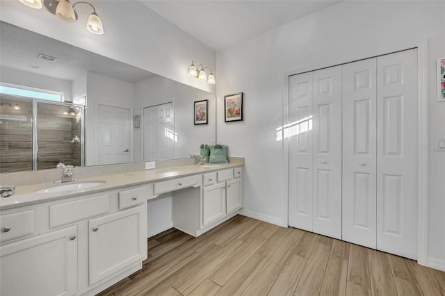 bathroom featuring wood finished floors, a sink, tiled shower, a closet, and double vanity