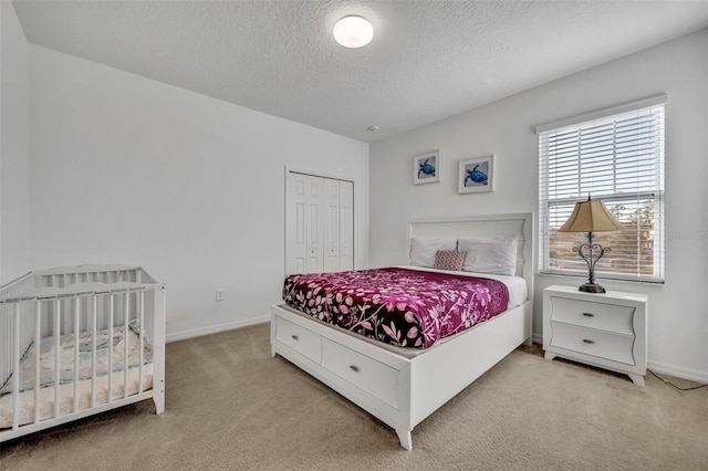 bedroom featuring light carpet, a closet, a textured ceiling, and baseboards