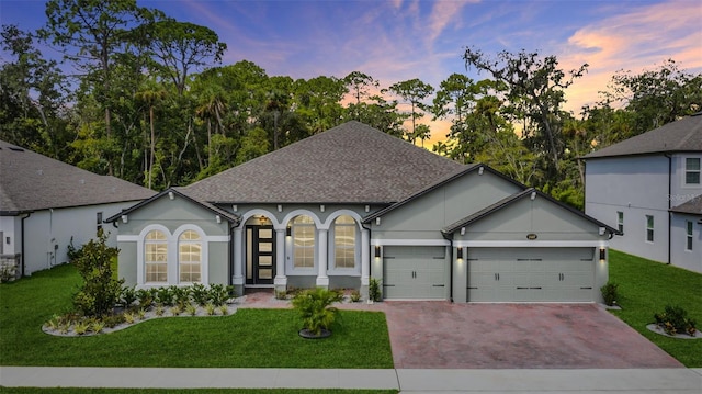 single story home featuring stucco siding, a lawn, decorative driveway, a shingled roof, and a garage