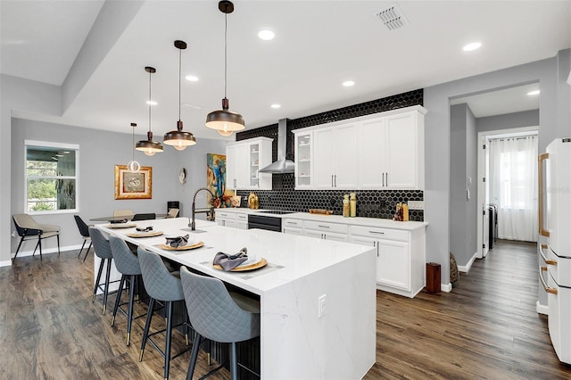 kitchen featuring decorative light fixtures, wall chimney exhaust hood, dark wood-type flooring, a kitchen bar, and a center island with sink