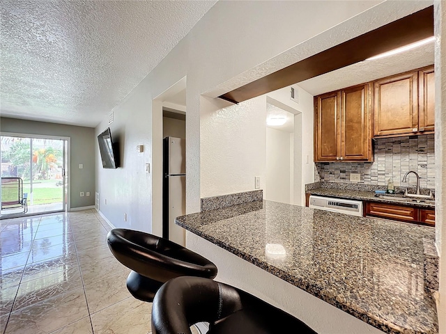 kitchen with dark stone counters, backsplash, sink, and stainless steel refrigerator