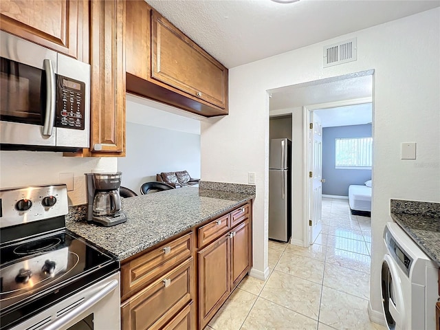 kitchen with dark stone counters, washer / clothes dryer, appliances with stainless steel finishes, and light tile patterned floors