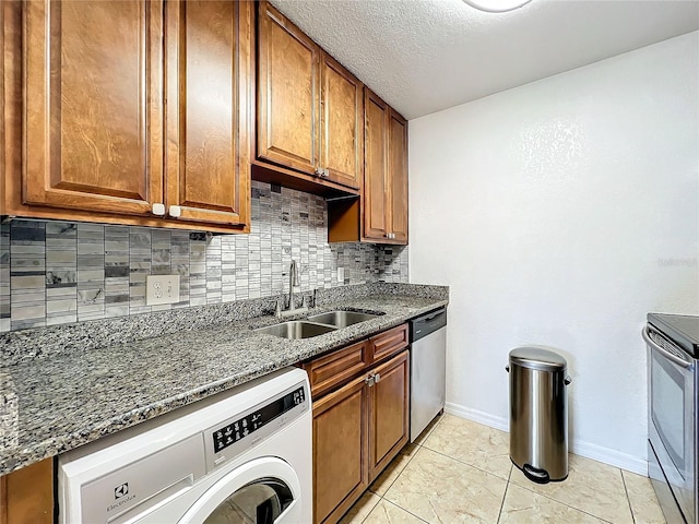 kitchen with stainless steel appliances, tasteful backsplash, sink, washer / clothes dryer, and dark stone countertops