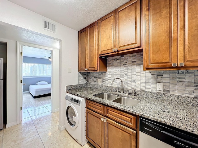 kitchen featuring sink, stone counters, stainless steel dishwasher, and washer / dryer