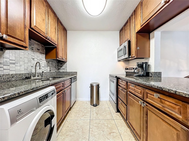 kitchen with stainless steel appliances, sink, washer / clothes dryer, light tile patterned floors, and dark stone counters