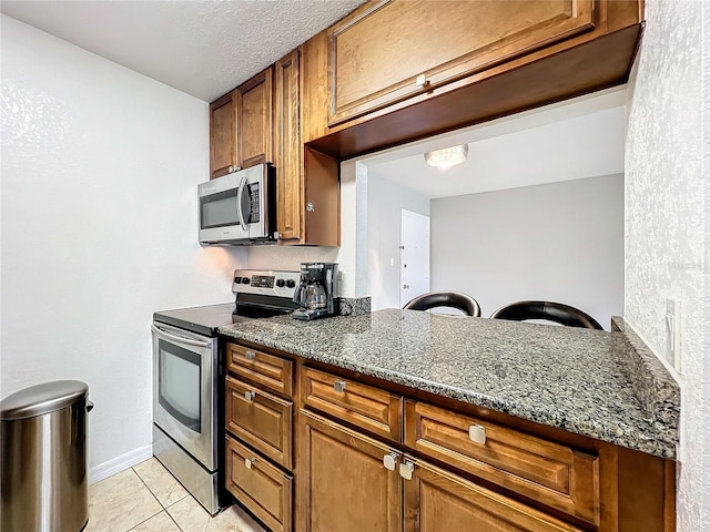 kitchen with dark stone counters, stainless steel appliances, light tile patterned flooring, and kitchen peninsula