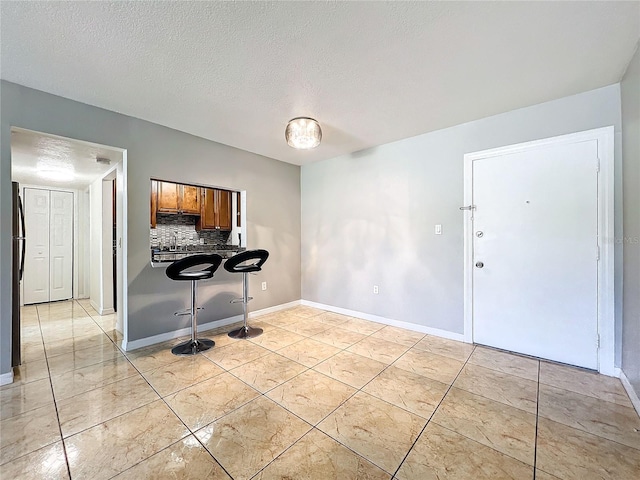 interior space featuring a textured ceiling, decorative backsplash, light tile patterned floors, and a kitchen breakfast bar