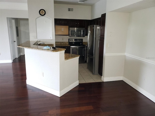 kitchen featuring visible vents, dark wood-type flooring, a peninsula, light stone countertops, and stainless steel appliances