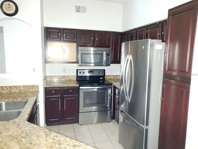 kitchen featuring visible vents, light stone countertops, stainless steel appliances, a sink, and light tile patterned flooring