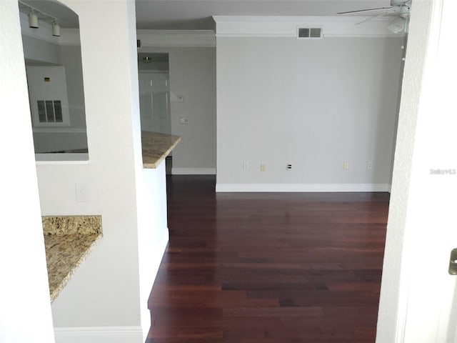 empty room featuring ceiling fan, dark wood-style flooring, visible vents, baseboards, and ornamental molding