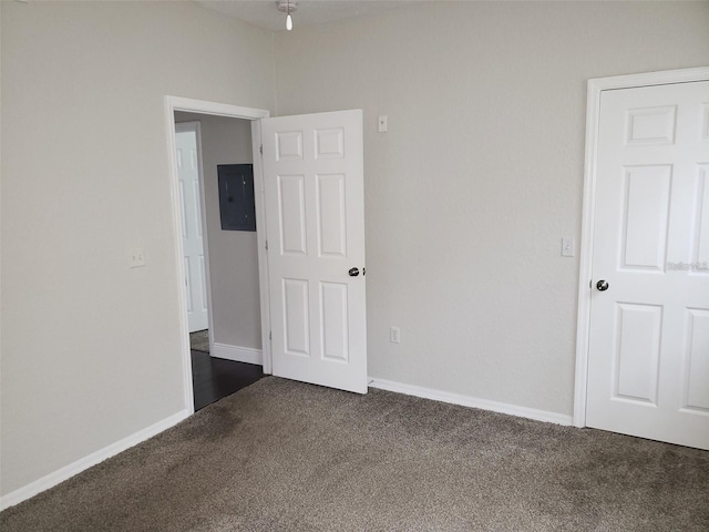 unfurnished bedroom with dark colored carpet, electric panel, and baseboards