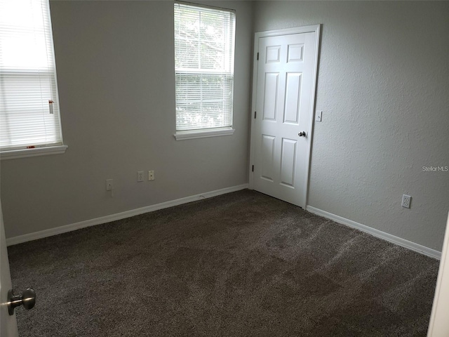 empty room featuring baseboards and dark colored carpet