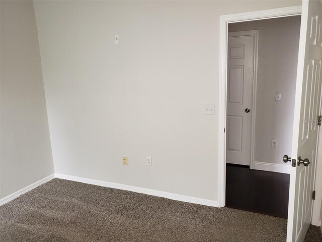 empty room featuring baseboards and dark carpet