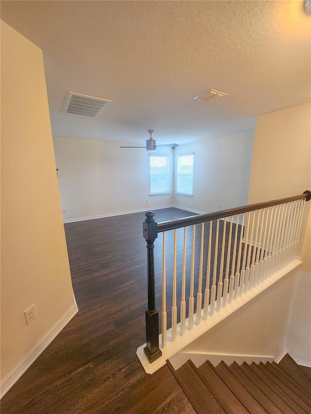 stairs with hardwood / wood-style floors, a textured ceiling, and ceiling fan