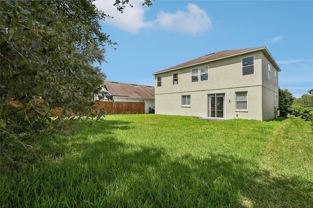 back of house with a lawn, fence, and stucco siding