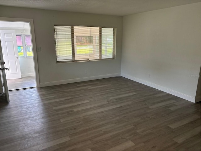 spare room with a textured ceiling, baseboards, and dark wood-style flooring