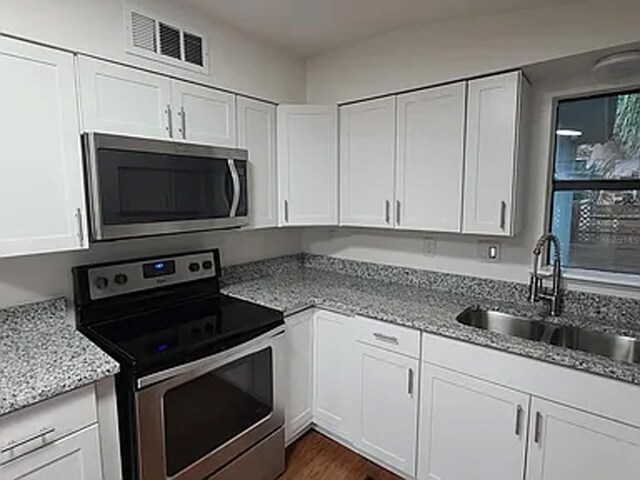 kitchen featuring appliances with stainless steel finishes, light stone counters, white cabinetry, and sink