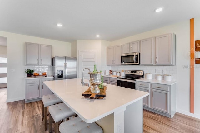 kitchen with a kitchen breakfast bar, decorative backsplash, a kitchen island with sink, and stainless steel appliances