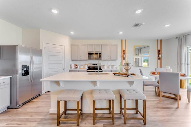 kitchen with a breakfast bar, an island with sink, and appliances with stainless steel finishes