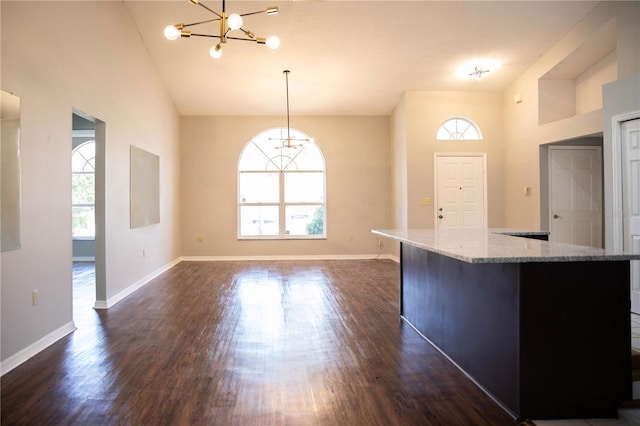 kitchen with a high ceiling, an inviting chandelier, light stone countertops, dark hardwood / wood-style floors, and pendant lighting