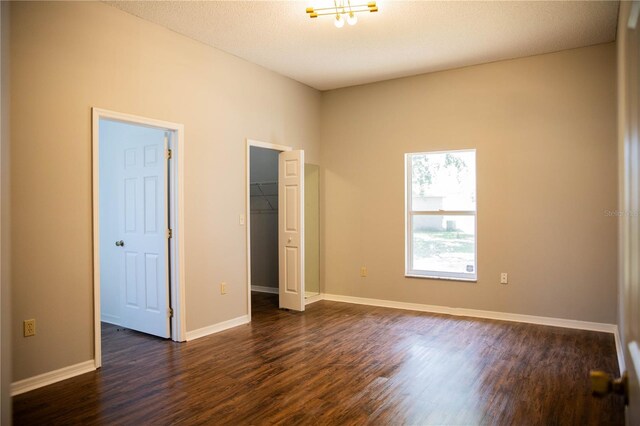 unfurnished bedroom with dark wood-type flooring, a closet, a walk in closet, and baseboards