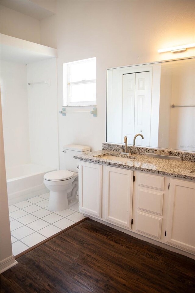 bathroom with a closet, toilet, vanity, wood finished floors, and  shower combination