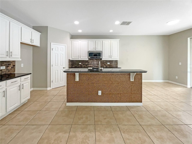 kitchen featuring dark countertops, stainless steel microwave, a kitchen breakfast bar, and a kitchen island with sink