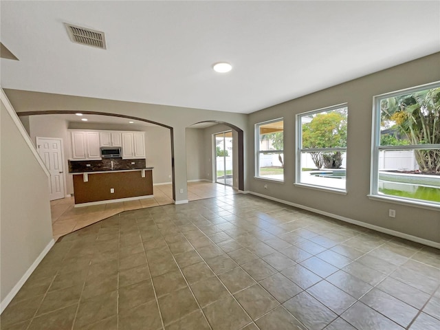 unfurnished living room featuring light tile patterned floors, baseboards, visible vents, and arched walkways