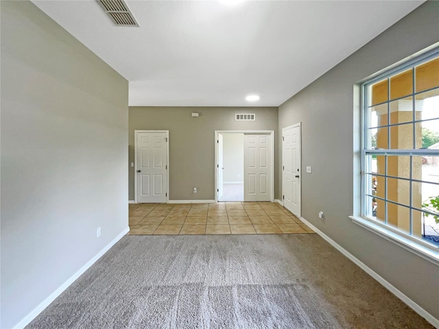 empty room with light tile patterned floors, plenty of natural light, visible vents, and baseboards