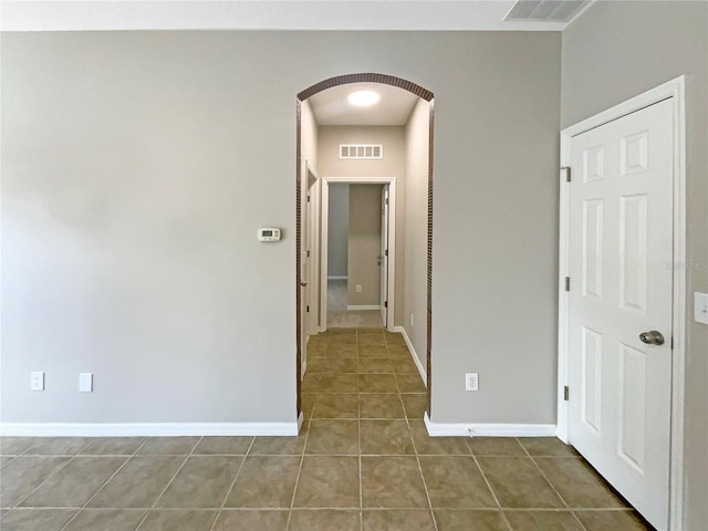 hall featuring arched walkways, dark tile patterned floors, visible vents, and baseboards