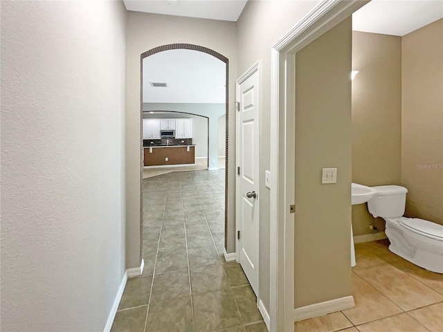 hall with arched walkways, tile patterned flooring, visible vents, and baseboards