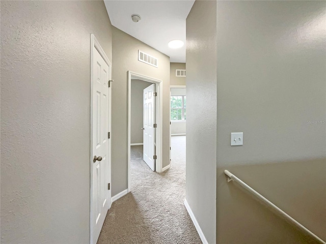 hall featuring an upstairs landing, baseboards, visible vents, and carpet flooring