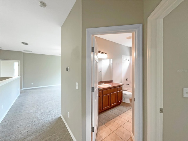 hallway with light tile patterned floors, visible vents, light carpet, a sink, and baseboards