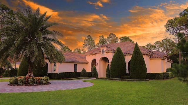 mediterranean / spanish home featuring a yard, a tiled roof, and stucco siding