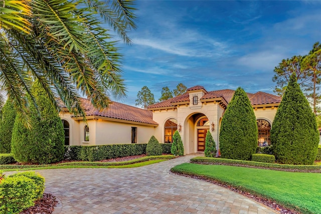 mediterranean / spanish-style house with a front lawn, a tile roof, and stucco siding