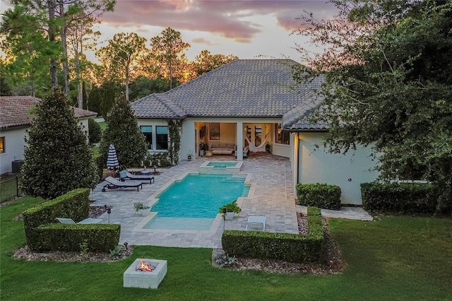 pool at dusk featuring a pool with connected hot tub, central AC unit, a lawn, and a patio