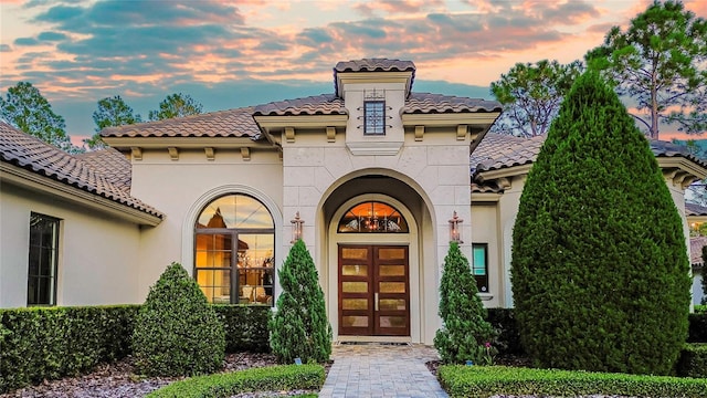 property entrance with a tile roof, french doors, and stucco siding