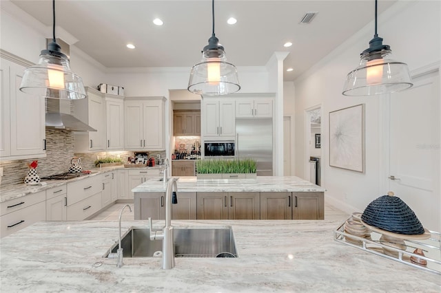 kitchen with visible vents, a kitchen island, a sink, built in appliances, and wall chimney exhaust hood